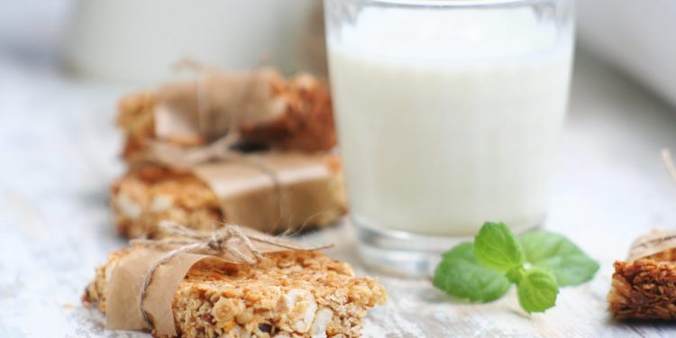 primo piano di barrette proteiche fatte in casa con la frutta secca e dietro un bicchiere di latte