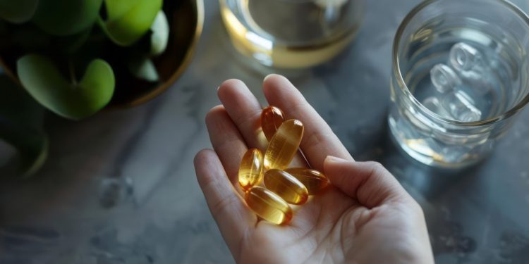 Mano di una donna con integratori per stanchezza fisica e mentale. In secondo piano un bicchiere di acqua e limoni