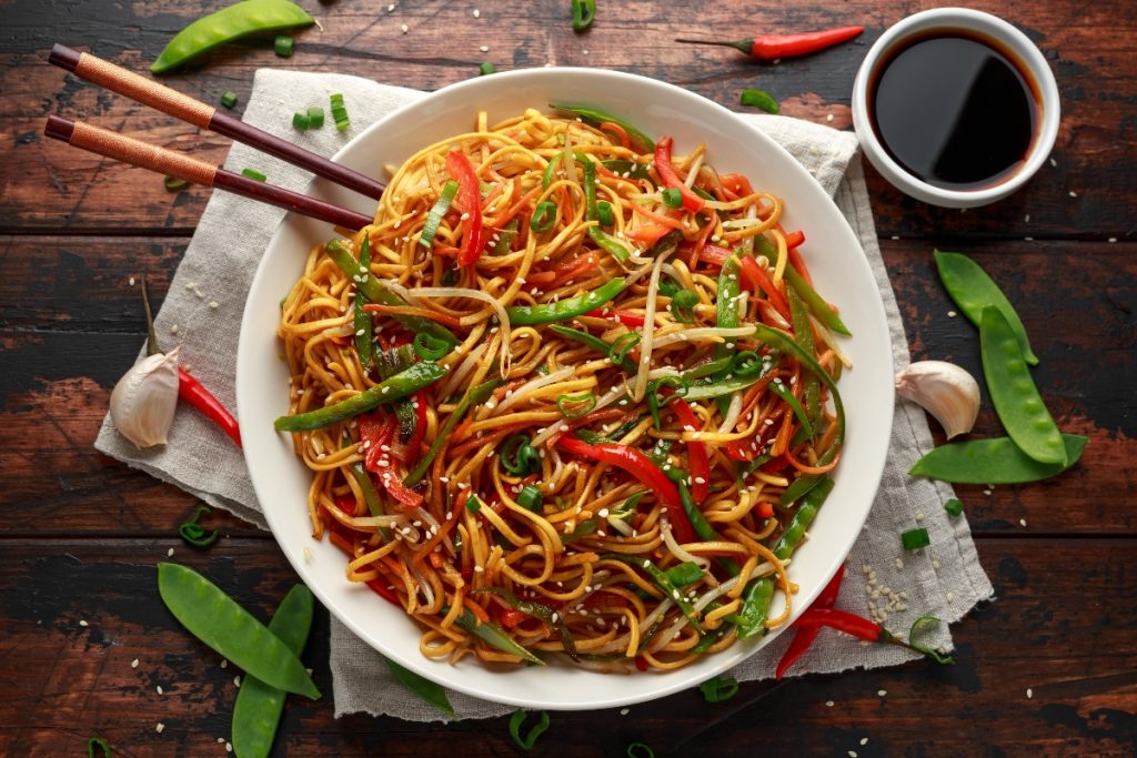 su tavolo di legno piatto di noodles con verdure e bacchette cinesi. Attorno edamame e salsa di soia