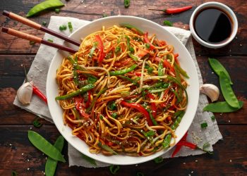 su tavolo di legno piatto di noodles con verdure e bacchette cinesi. Attorno edamame e salsa di soia