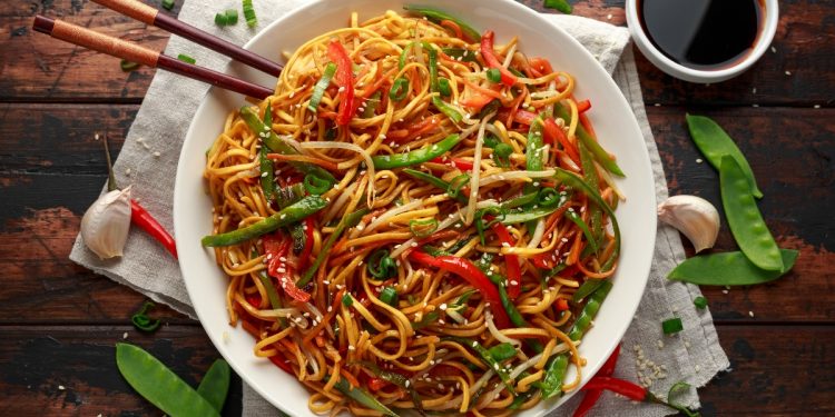 su tavolo di legno piatto di noodles con verdure e bacchette cinesi. Attorno edamame e salsa di soia