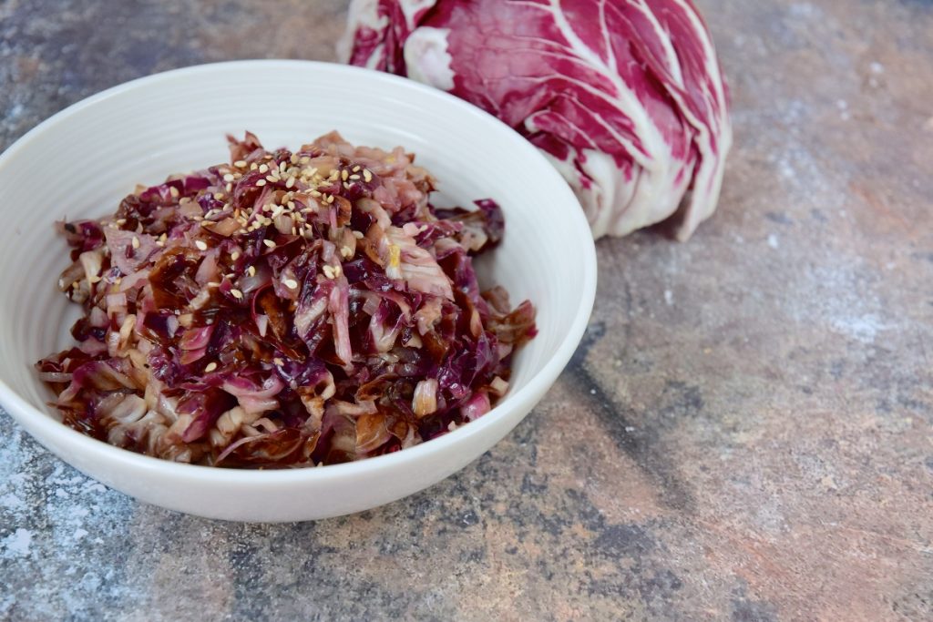 su tavolo di marmo, radicchio in padella in una ciotola bianca con semi di sesamo e dietro un radicchio