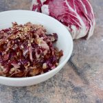 su tavolo di marmo, radicchio in padella in una ciotola bianca con semi di sesamo e dietro un radicchio