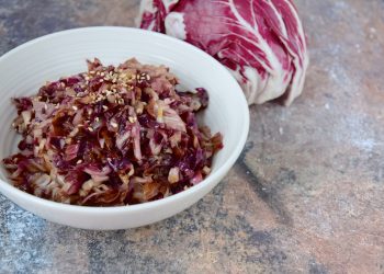 su tavolo di marmo, radicchio in padella in una ciotola bianca con semi di sesamo e dietro un radicchio