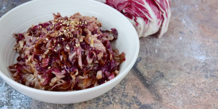 su tavolo di marmo, radicchio in padella in una ciotola bianca con semi di sesamo e dietro un radicchio