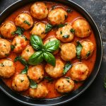 su tavolo da cucina nero primo piano di una padella con gnudi al pomodoro e attorno foglie di basilico e pepe nero