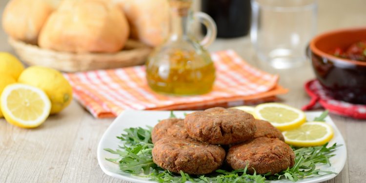 su tavolo da cucina, piatto con rucola, limoni tagliati e mondeghili, dietro una bottiglietta di olio EVO e panini