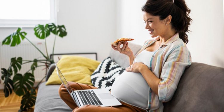 una donna in gravidanza che mangia una pizza con la mortadella