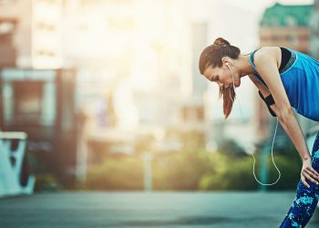 su un ponte di una città, donna stanca dopo corsa troppo veloce per overtraining che cerca di recuperare per riprendere fiato