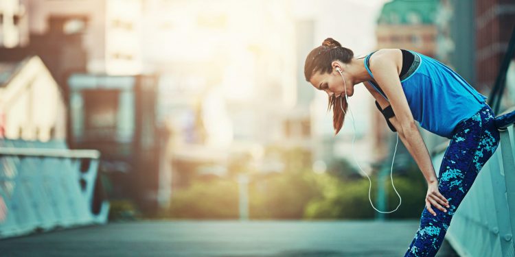 su un ponte di una città, donna stanca dopo corsa troppo veloce per overtraining che cerca di recuperare per riprendere fiato