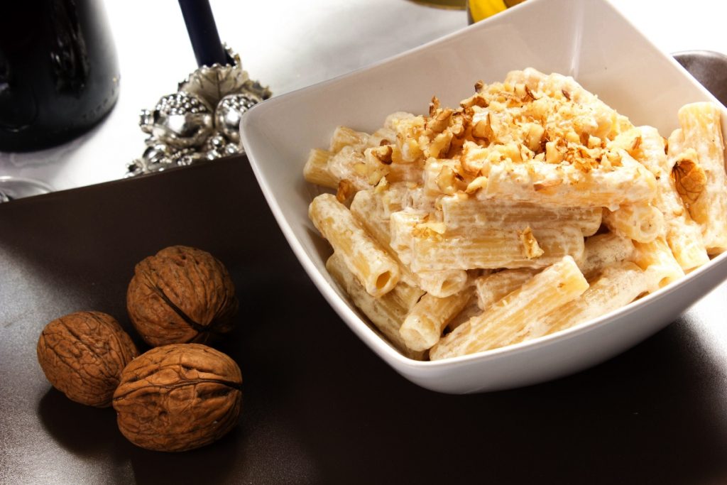 su tavolo un piatto bianco con pasta ricotta e noci accanto 3 noci e un bicchiere di vino bianco