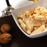 su tavolo un piatto bianco con pasta ricotta e noci accanto 3 noci e un bicchiere di vino bianco