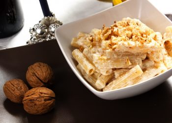 su tavolo un piatto bianco con pasta ricotta e noci accanto 3 noci e un bicchiere di vino bianco