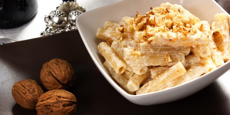 su tavolo un piatto bianco con pasta ricotta e noci accanto 3 noci e un bicchiere di vino bianco