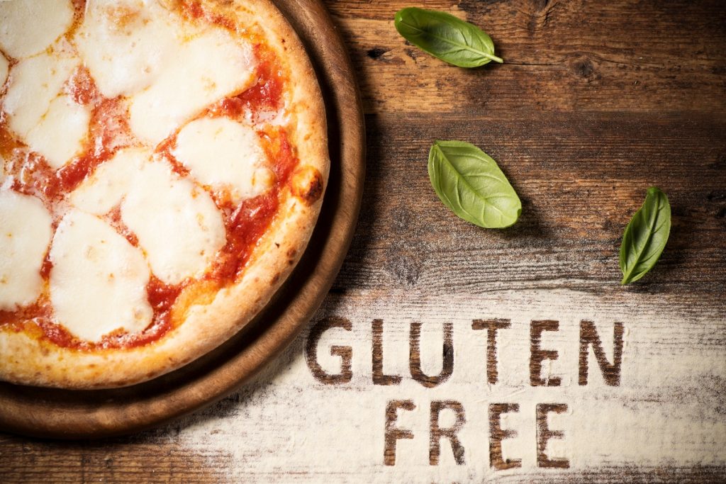 su tavolo di legno: farina sparsa e basilico con a sinistra metà di una pizza senza glutine con a destra la scritta gluten free