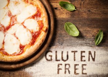 su tavolo di legno: farina sparsa e basilico con a sinistra metà di una pizza senza glutine con a destra la scritta gluten free