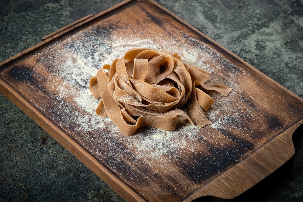 Su tavolo di marmo, tagliere con tagliatelle con farina di castagne appena fatte e farina