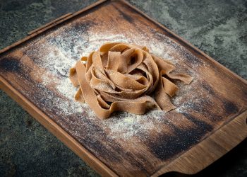 Su tavolo di marmo, tagliere con tagliatelle con farina di castagne appena fatte e farina