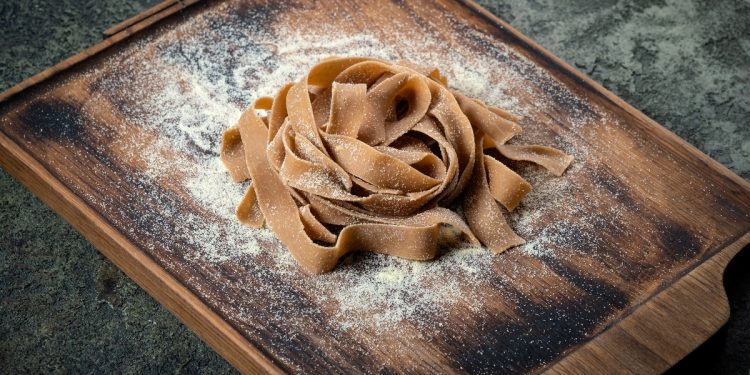 Su tavolo di marmo, tagliere con tagliatelle con farina di castagne appena fatte e farina