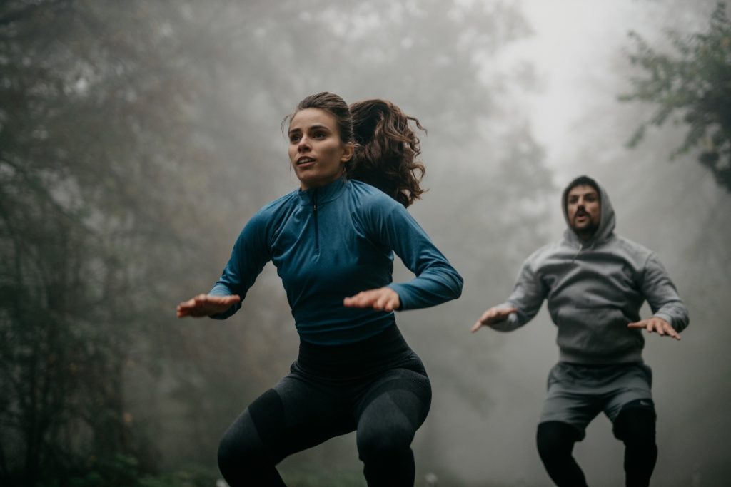 In un bosco con la nebbia una coppia che eseguono salti durante un workout HIIT