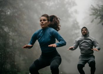 In un bosco con la nebbia una coppia che eseguono salti durante un workout HIIT