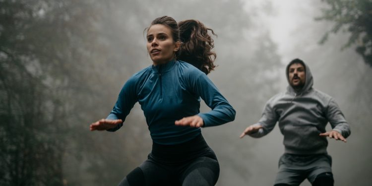 In un bosco con la nebbia una coppia che eseguono salti durante un workout HIIT