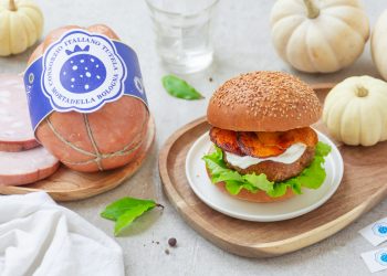 Burger con mortadella posizionato su un piatto di legno e accompagnato da elementi di decorazione