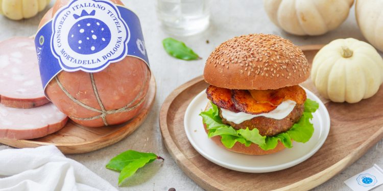 Burger con mortadella posizionato su un piatto di legno e accompagnato da elementi di decorazione