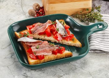 su tavolo da cucina di marmo, in una padella rettangolare un toast tagliato a triangolo con pomodorini