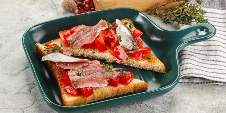 su tavolo da cucina di marmo, in una padella rettangolare un toast tagliato a triangolo con pomodorini