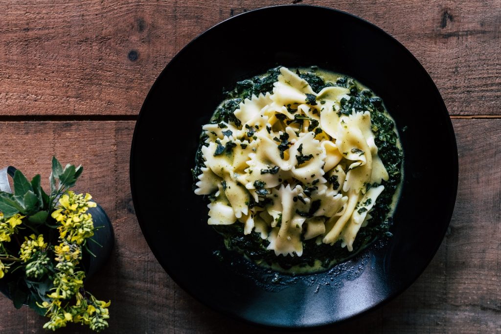 su tavolo di legno, piatto nero con pasta con spinaci freschi. A sinistra una pianta con fiori