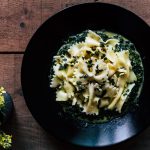 su tavolo di legno, piatto nero con pasta con spinaci freschi. A sinistra una pianta con fiori