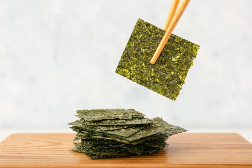 su tavolo tagliere di legno con fogli di alga Nori e un foglio in alto con le bacchette cinesi