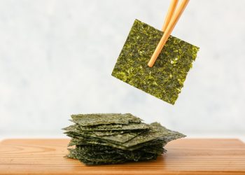 su tavolo tagliere di legno con fogli di alga Nori e un foglio in alto con le bacchette cinesi