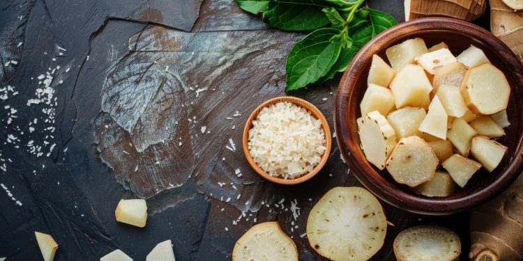 su tavolo nero, ciotola con manioca tagliata a fette con altre fette della radice sparse sul tavolo e erbe aromatiche