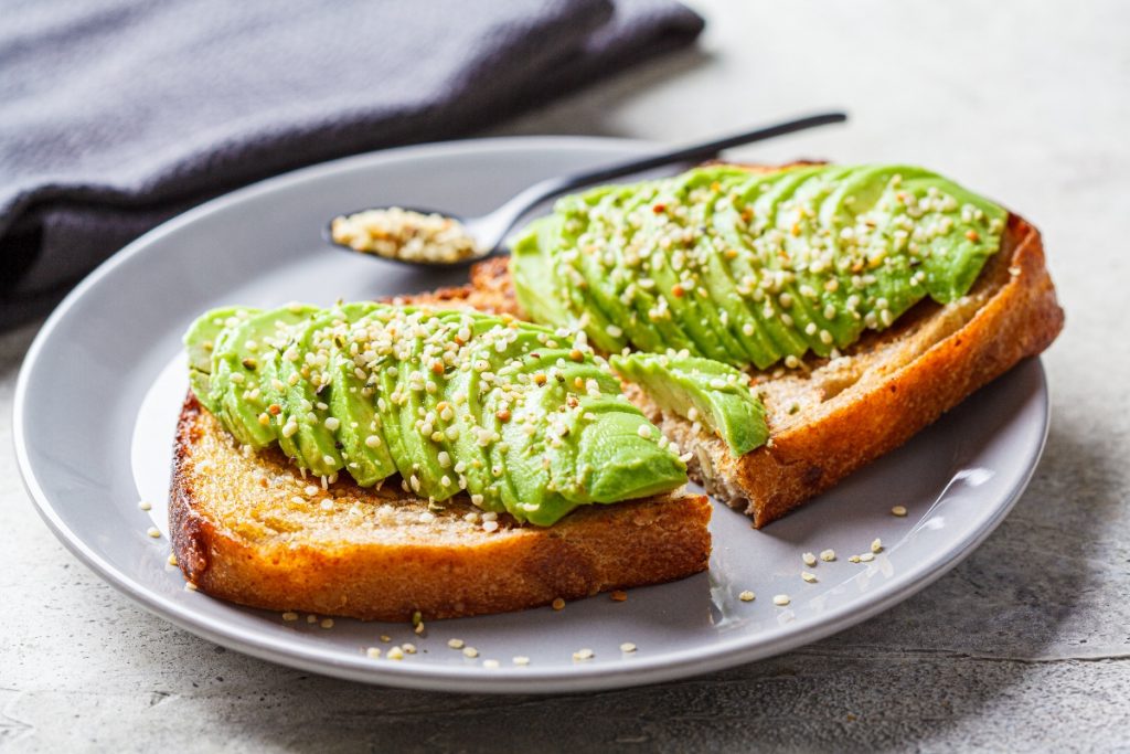 su tavolo di legno grigio, toast con avocado e semi di canapa e un cucchiaino. Dietro tovagliolo grigio