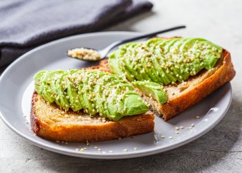 su tavolo di legno grigio, toast con avocado e semi di canapa e un cucchiaino. Dietro tovagliolo grigio