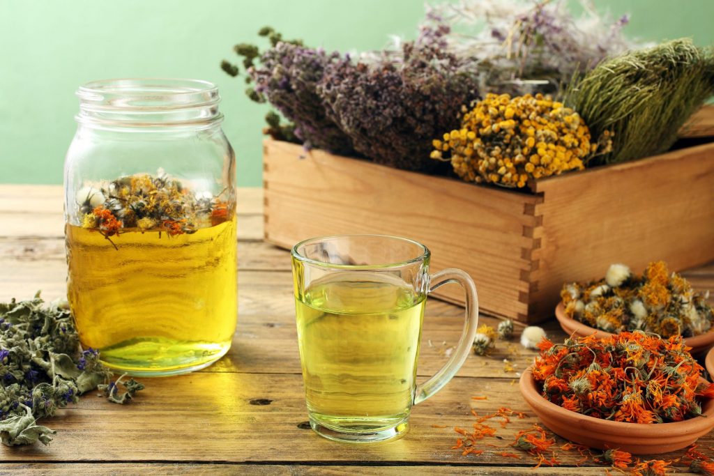 su tavolo di legno, scatola di legno con erbe e piante, davanti un bicchiere grande e un bicchiere piccolo con tisane dimagranti pieni di erbe