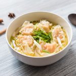 su tavolo di legno ciottola con i wonton in brodo e verdure, sulla sinistra bacchette cinesi e a destra cucchiaio di legno