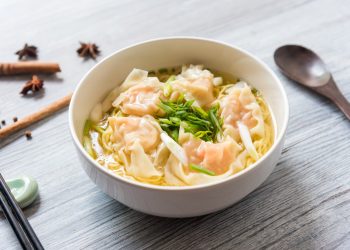 su tavolo di legno ciottola con i wonton in brodo e verdure, sulla sinistra bacchette cinesi e a destra cucchiaio di legno