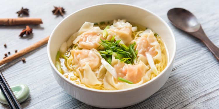 su tavolo di legno ciottola con i wonton in brodo e verdure, sulla sinistra bacchette cinesi e a destra cucchiaio di legno