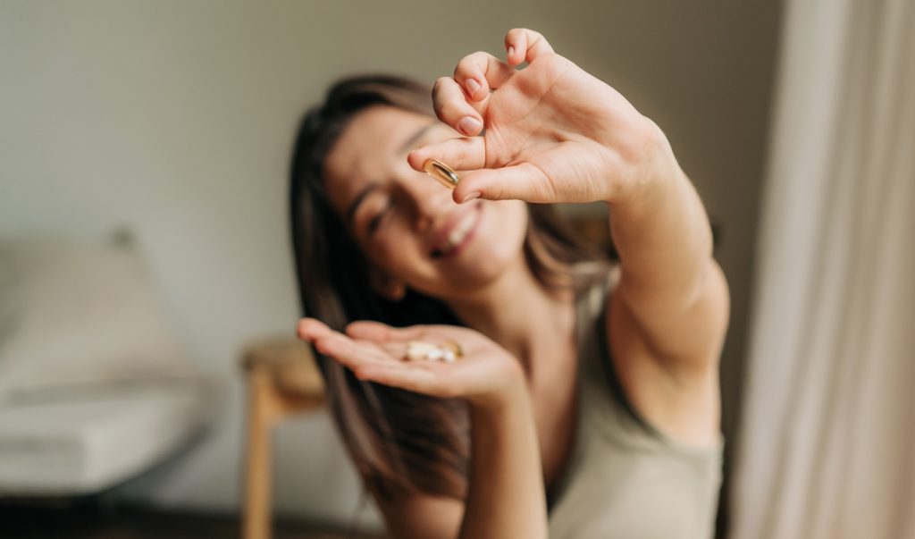 donna in soggiorno sorridente che tiene in mano integratori di fibre e fa vedere la pillola nell'altra mano