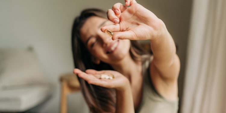 donna in soggiorno sorridente che tiene in mano integratori di fibre e fa vedere la pillola nell'altra mano