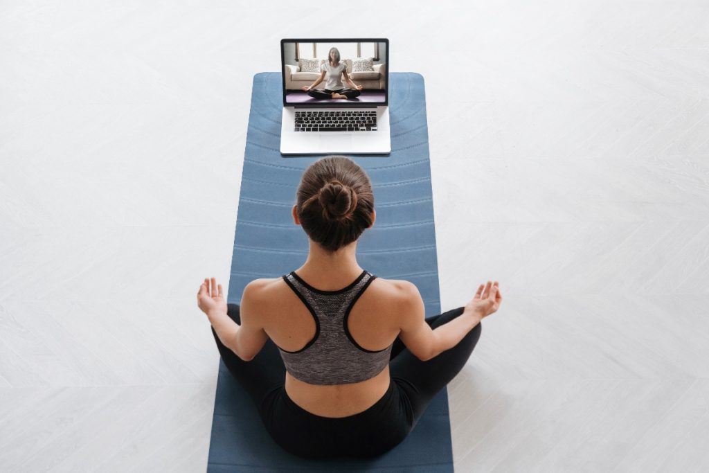 per un articolo su tappetini yoga, una donna seduta su un tappeto nella posizione semplice davanti ad un computer con una lezione di Yoga