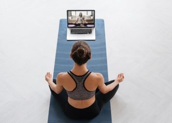 per un articolo su tappetini yoga, una donna seduta su un tappeto nella posizione semplice davanti ad un computer con una lezione di Yoga